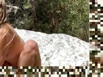 naked natural cute blonde model drinks water from a stream in nature
