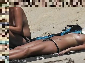 Topless ladies with tan lines relax in the sand