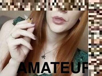 A red-haired girl with long hair smokes a cigarette with a brown